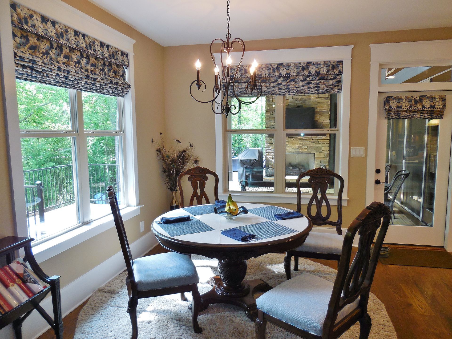 Bright dining room with round table, patterned chairs, large windows, and chandelier.