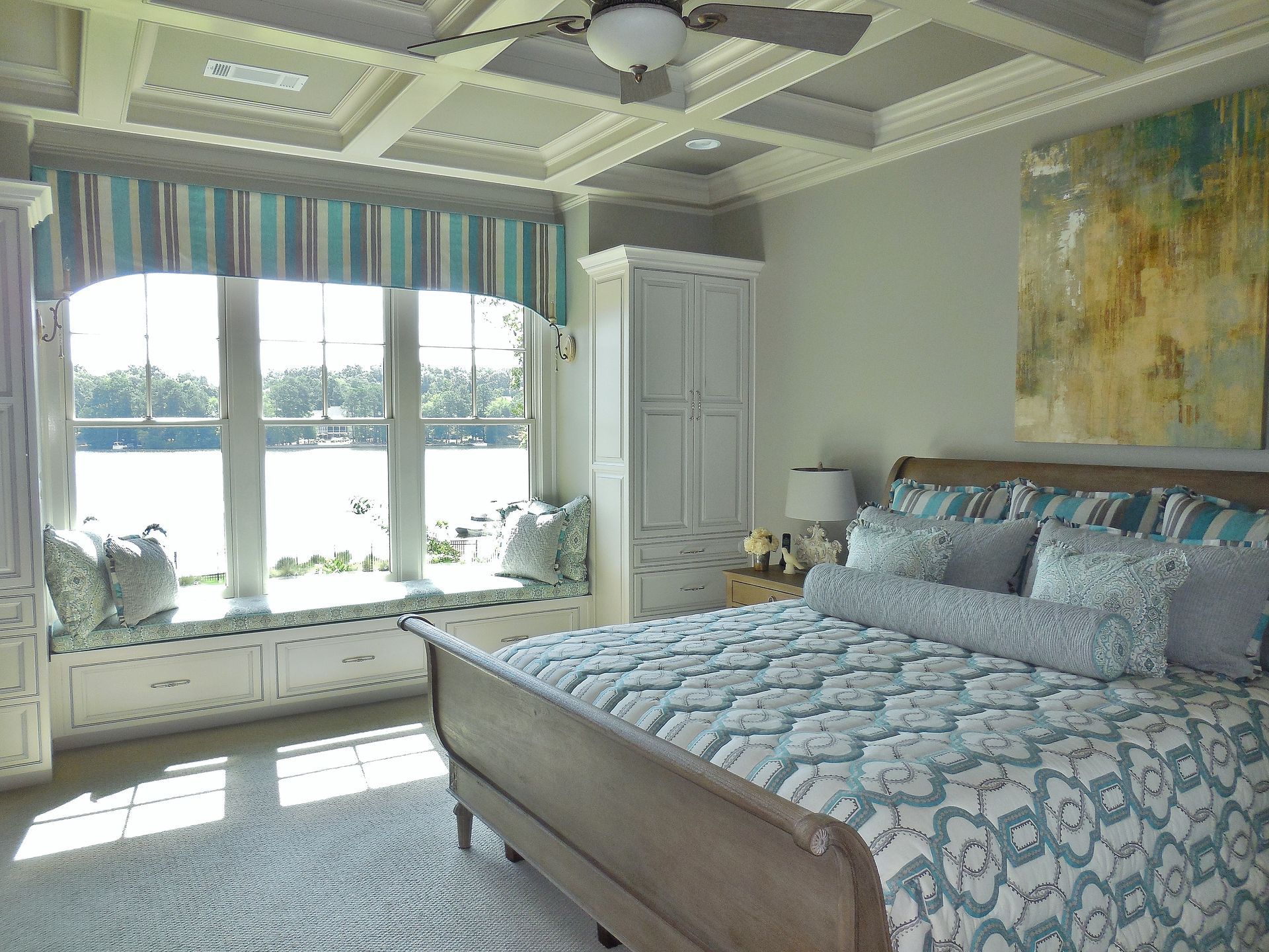 Bright bedroom with a large bed, bay window, and soft blue decor overlooking the water