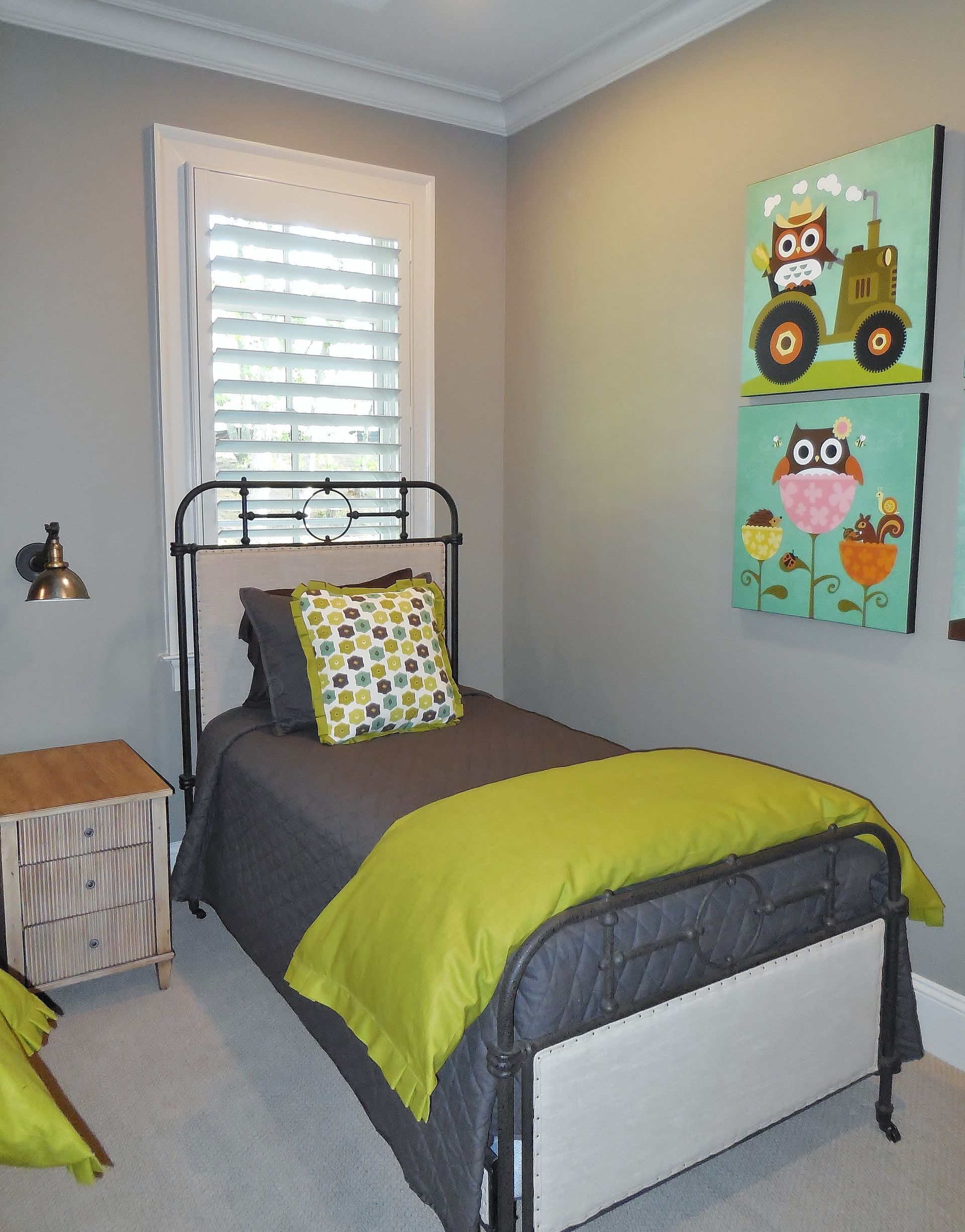 Small bedroom with twin bed, gray walls, owl wall art, green bedding, and a window with shutters.