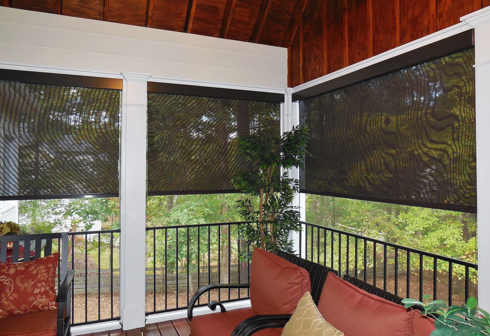 Porch with black roller shades, white columns, railing, and red cushioned seating under a wood ceiling