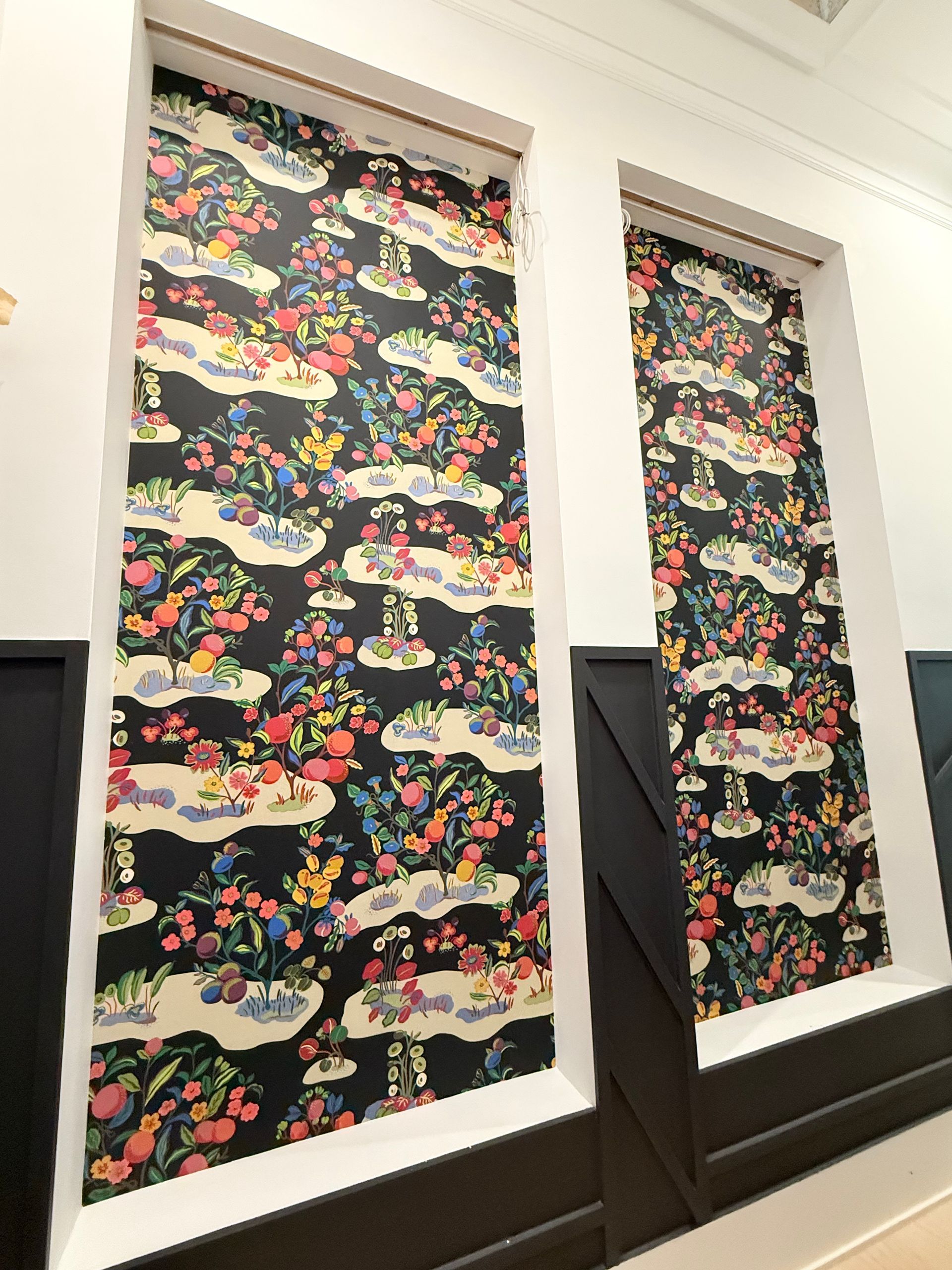 Two tall windows covered with black floral-patterned curtains in a white room