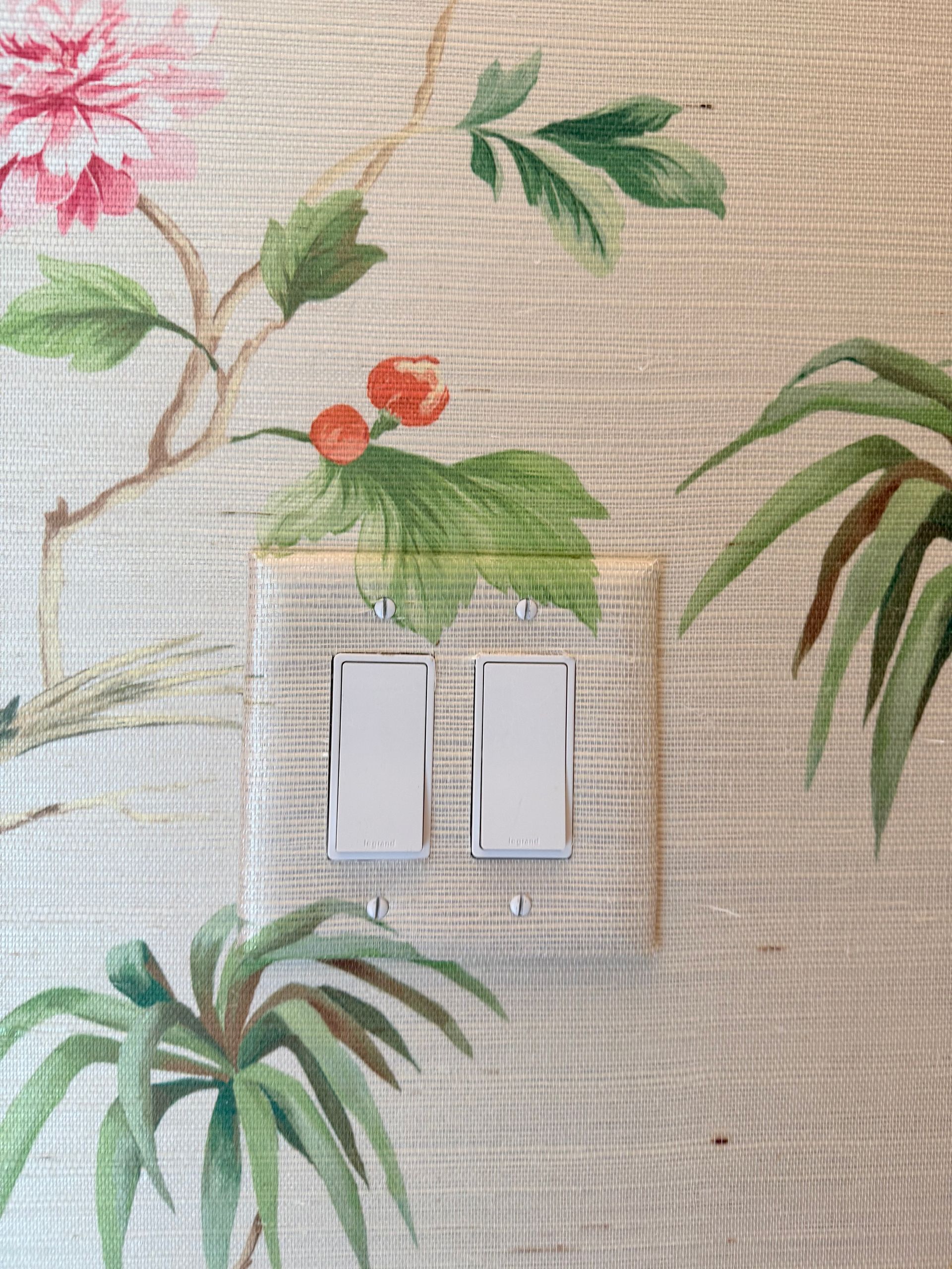 Two white light switches on a floral wallpapered wall