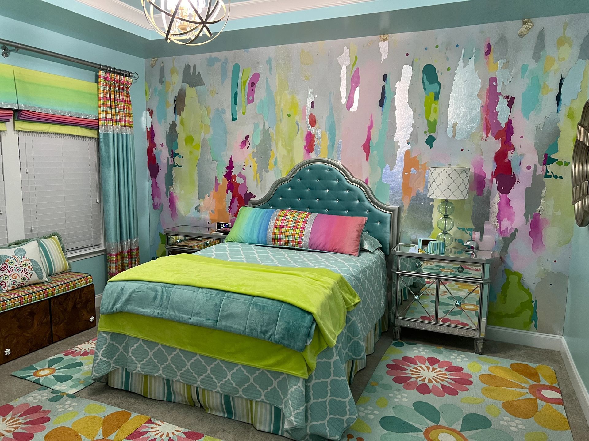 Bright colorful bedroom with patterned bedspread, teal tufted headboard, floral rug, and paint-splashed accent wall