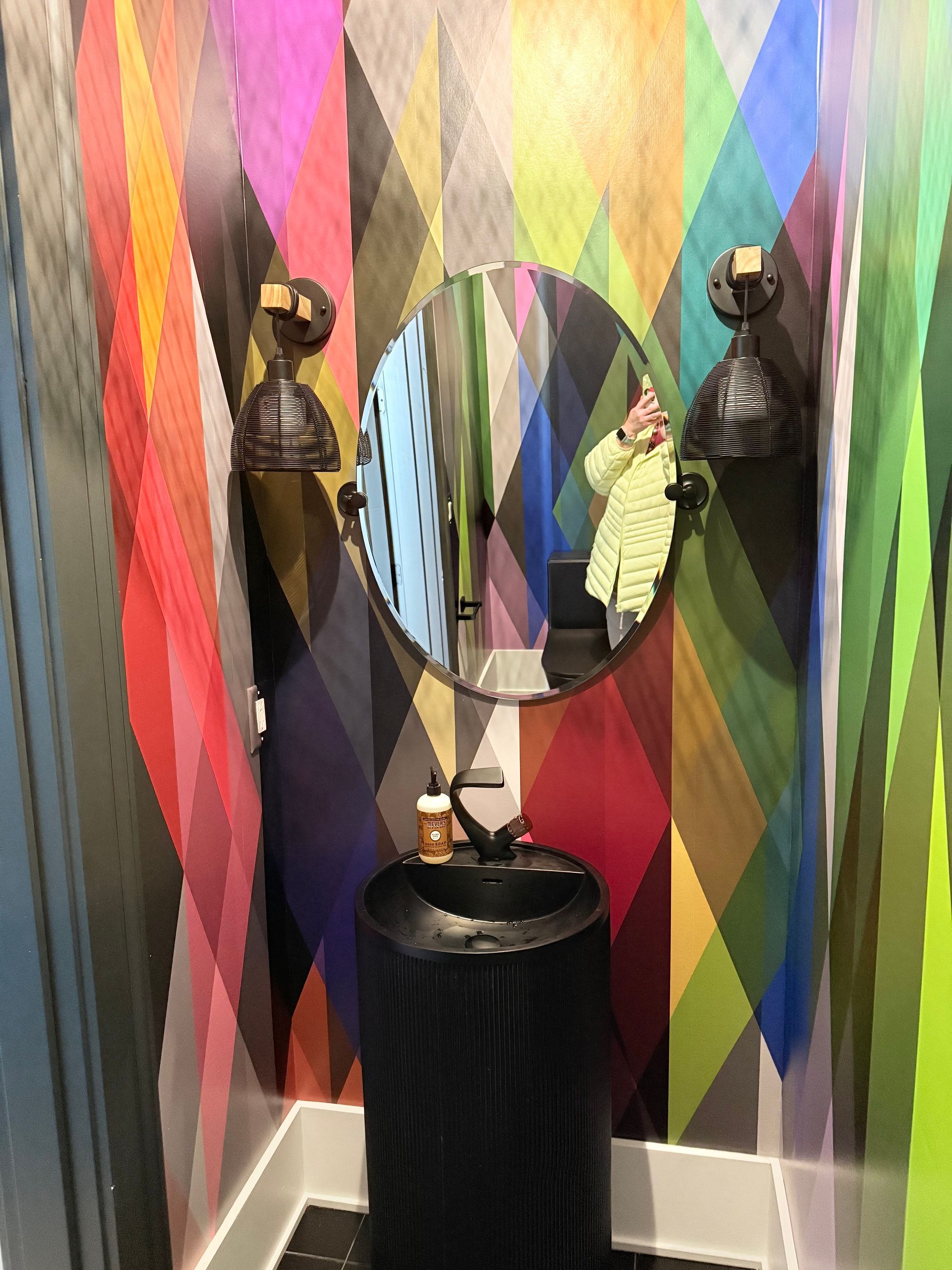 Colorful striped wall with a round mirror and decorative busts on a small black pedestal table