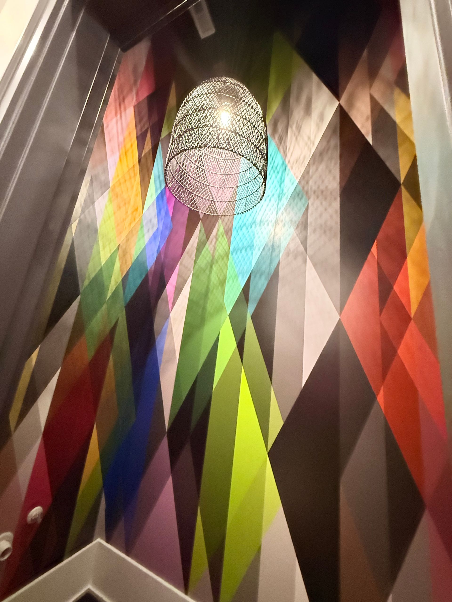 Colorful geometric wall art with a textured silver pendant light hanging overhead.
