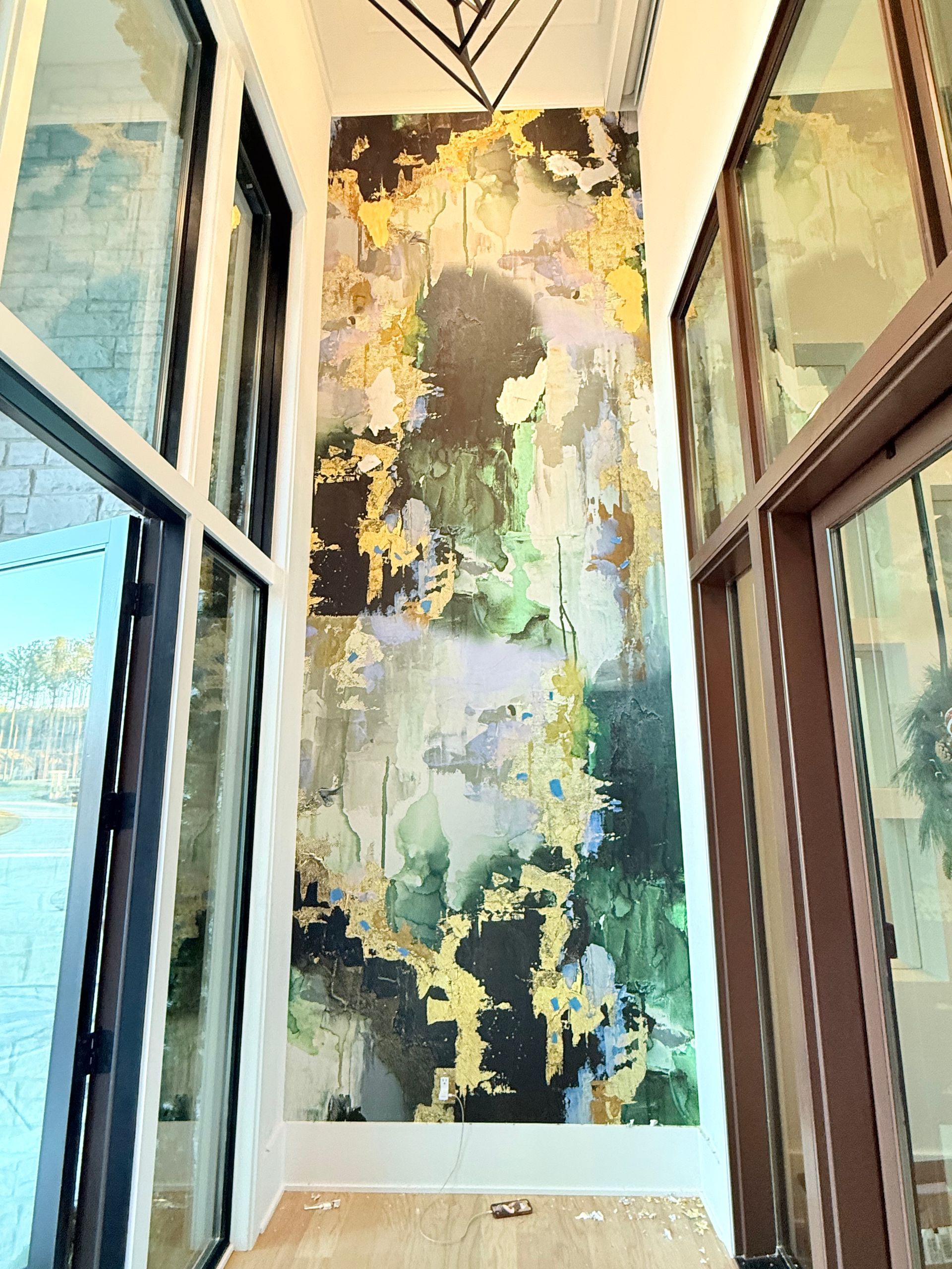 Tall abstract painting in a bright corner with large windows and glass doors.