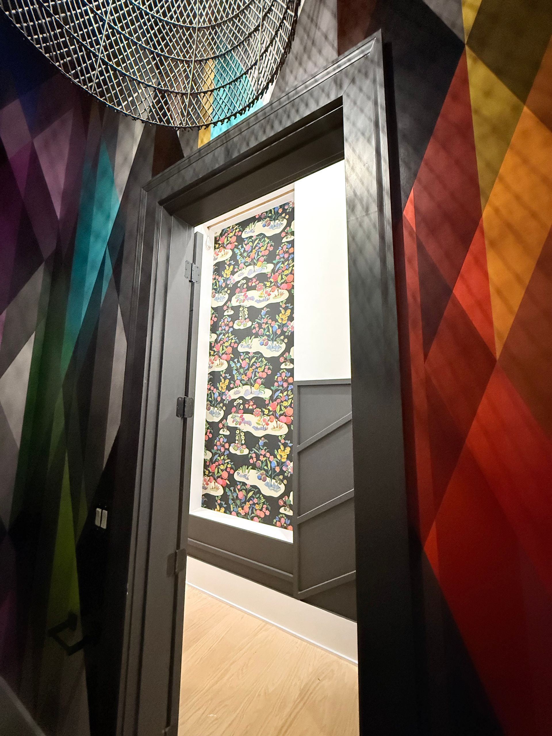Colorful patterned hallway with dark doorframe, geometric wall art, and a stairway visible through the doorway