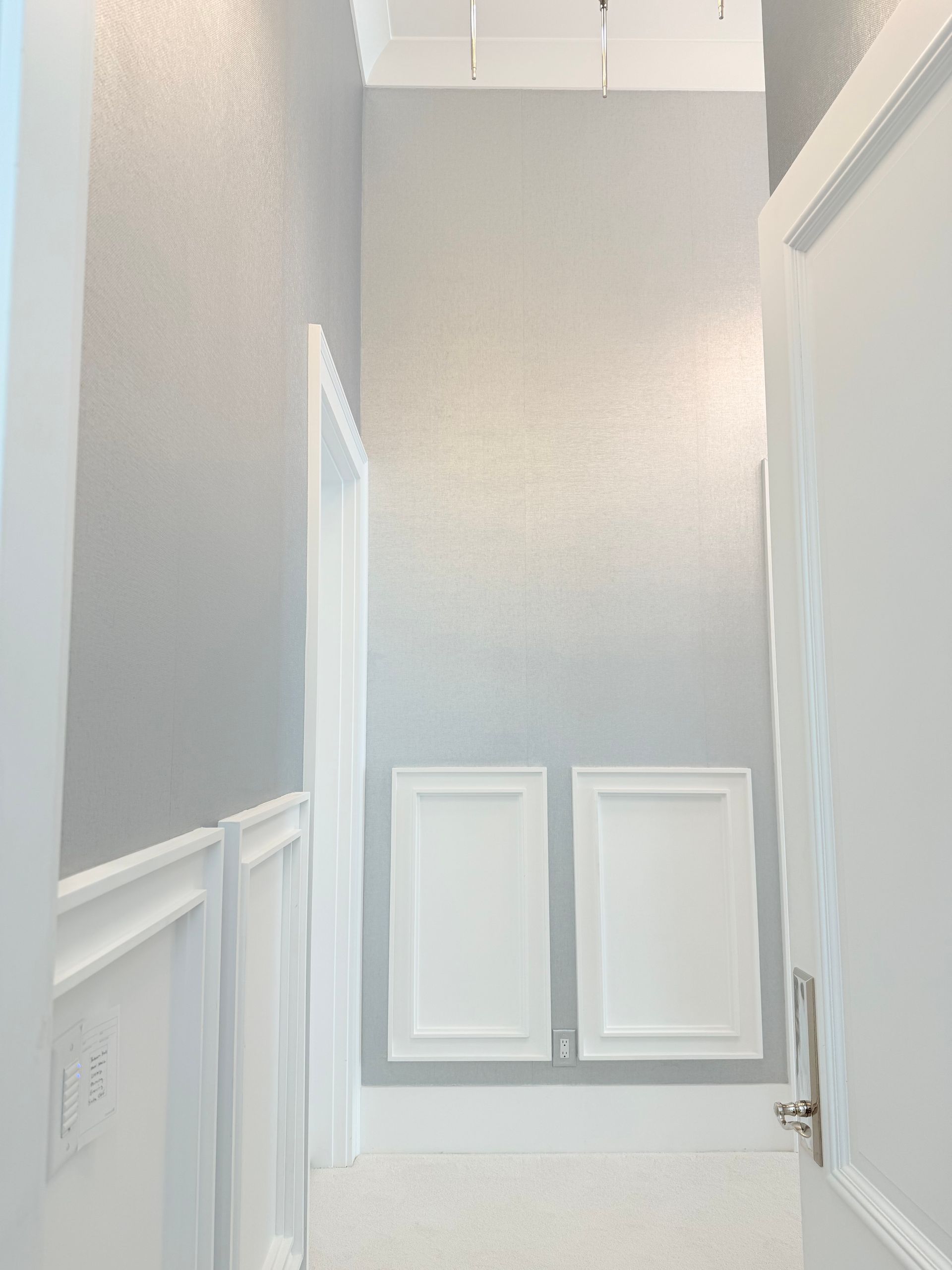 Narrow stairwell with gray walls, white trim, and two small rectangular wall panels or windows at the top.
