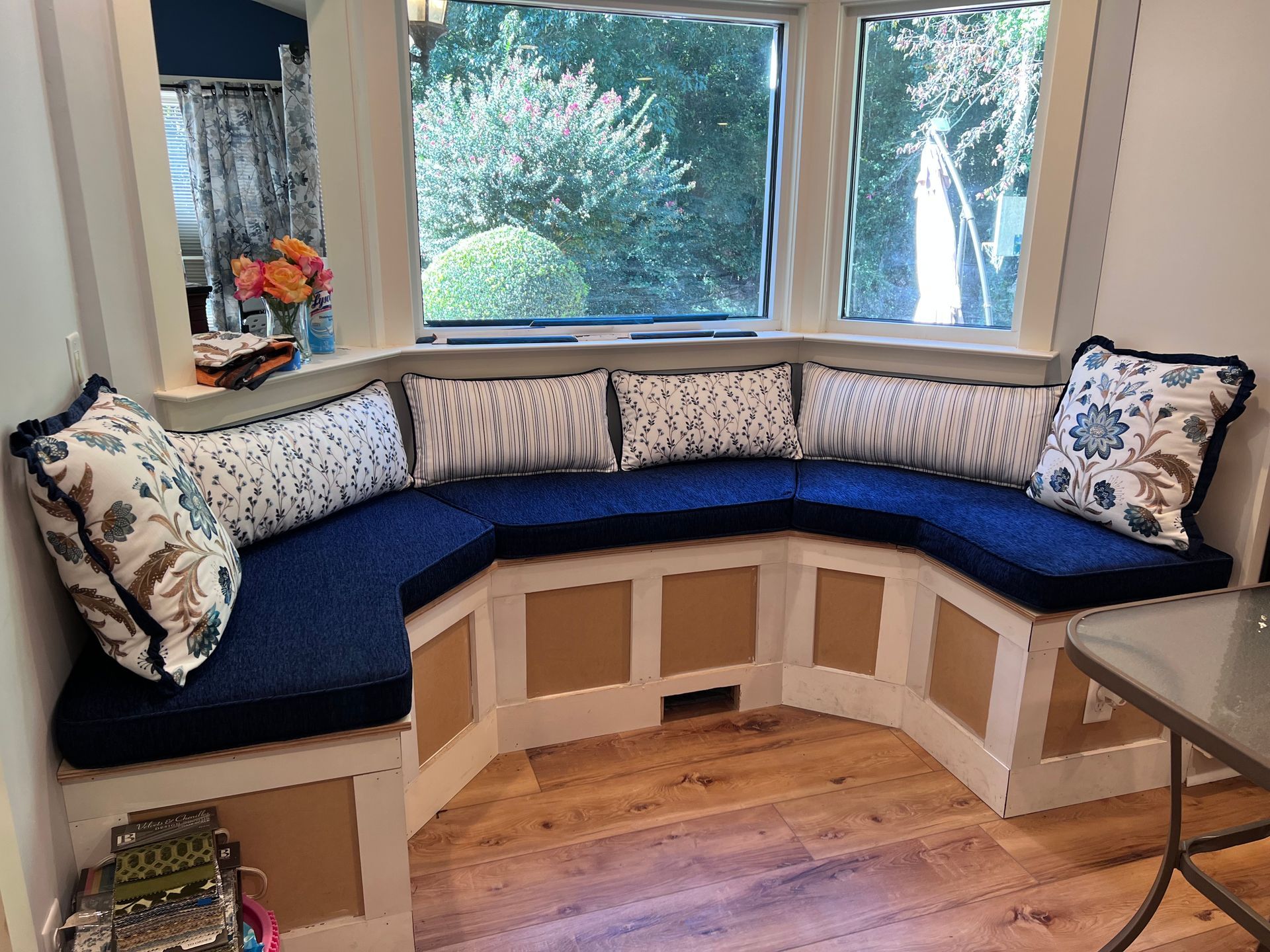 Built-in blue window seat with patterned cushions beneath a bay window in a bright room