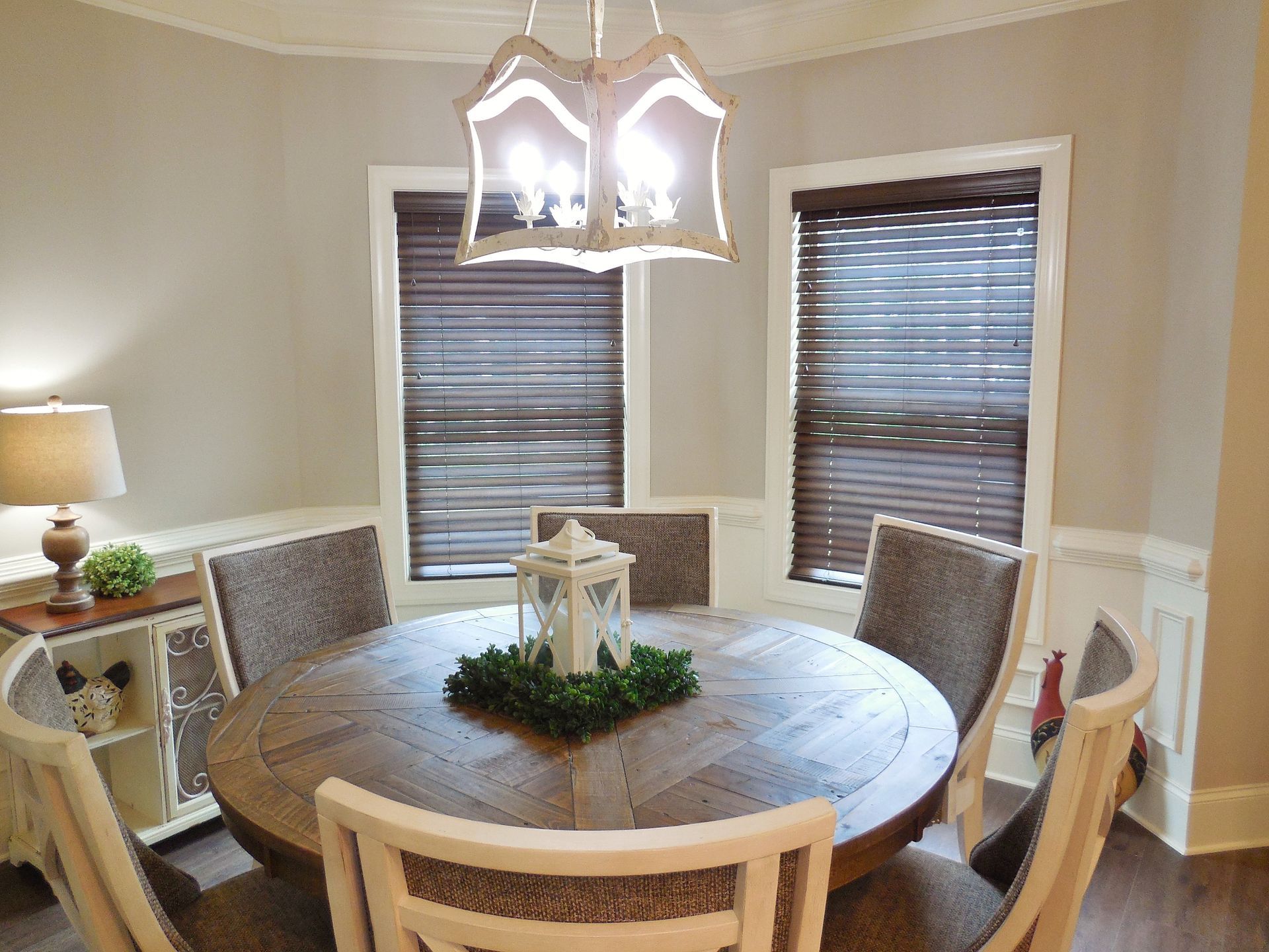 Round dining table with four chairs in a beige dining room with windows and a hanging light fixture