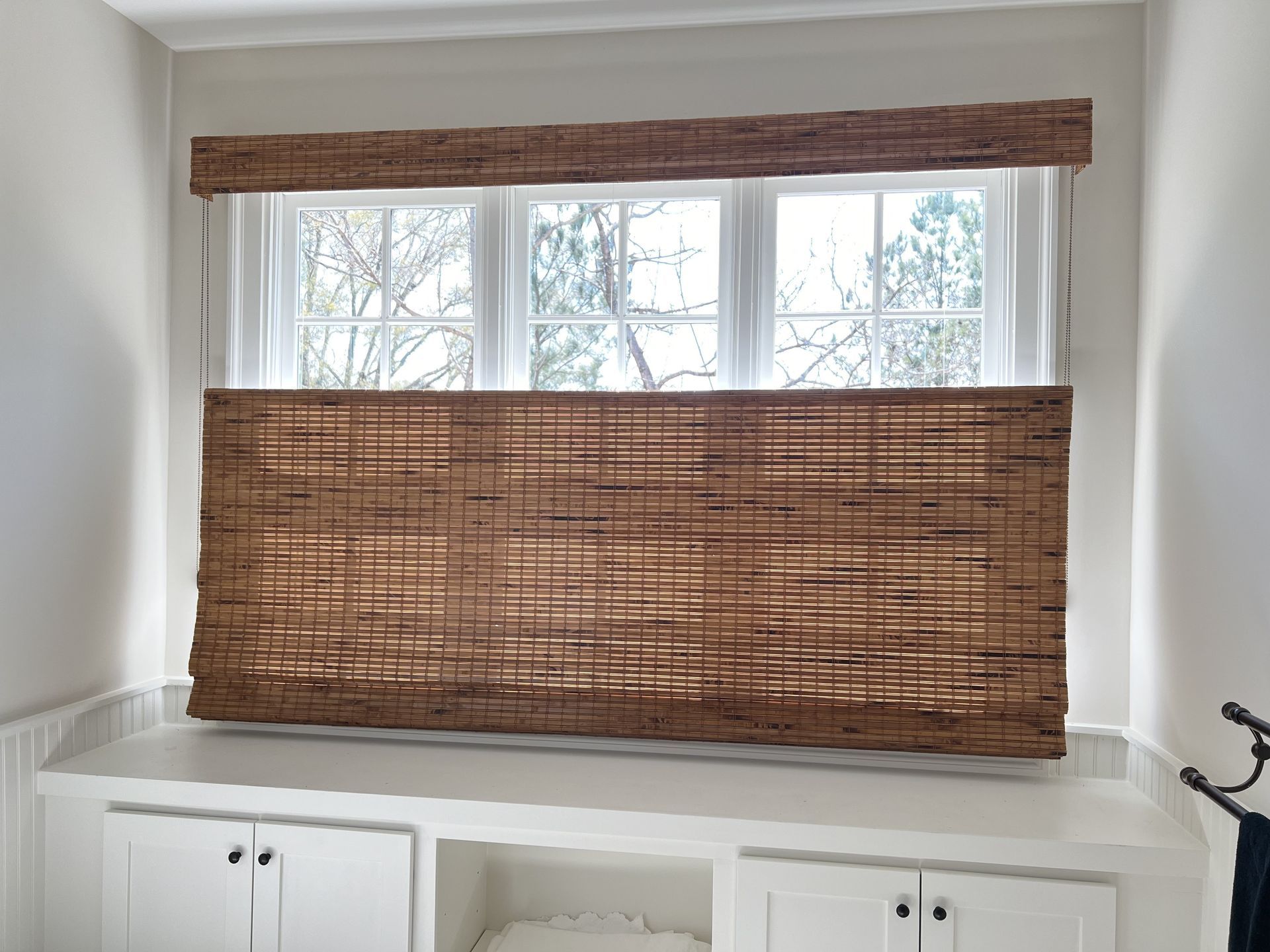 Window with bamboo shade and woven blind covering the lower half, above white built-in cabinets.