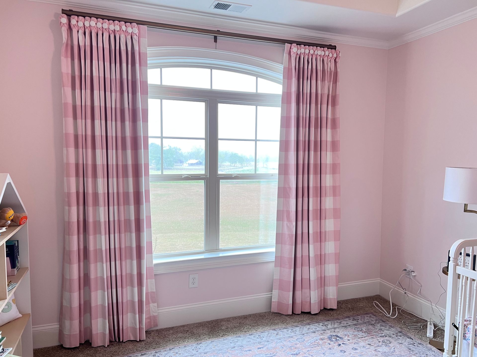 Pink bedroom with checkered curtains, a large window, and a pink patterned rug
