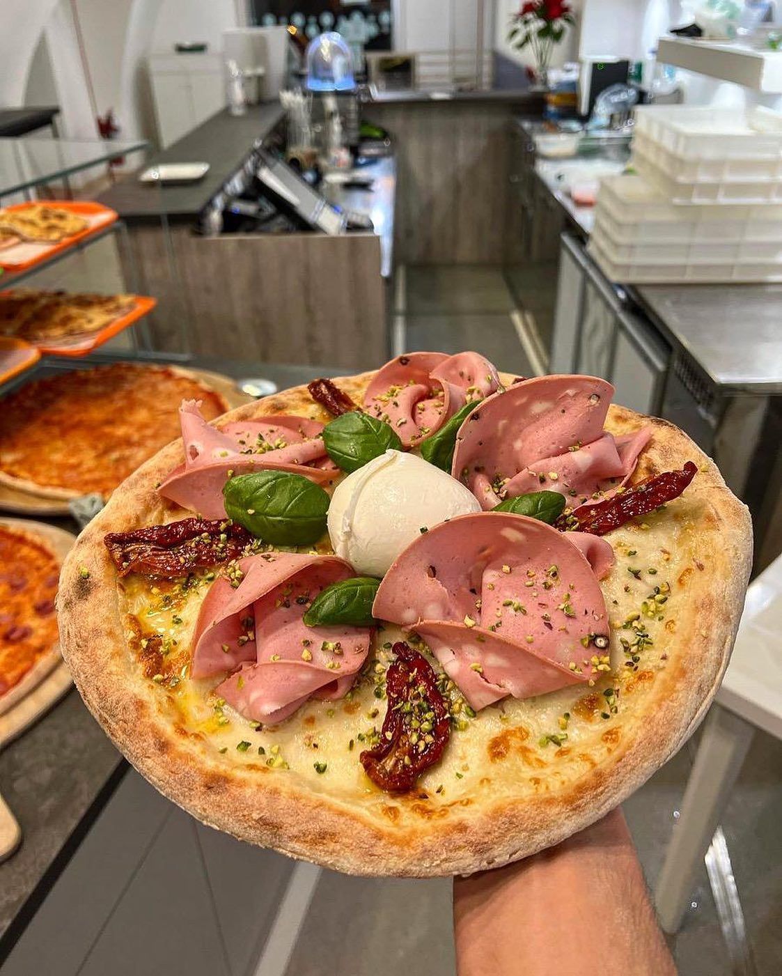 Una persona tiene una pizza in mano in una cucina.