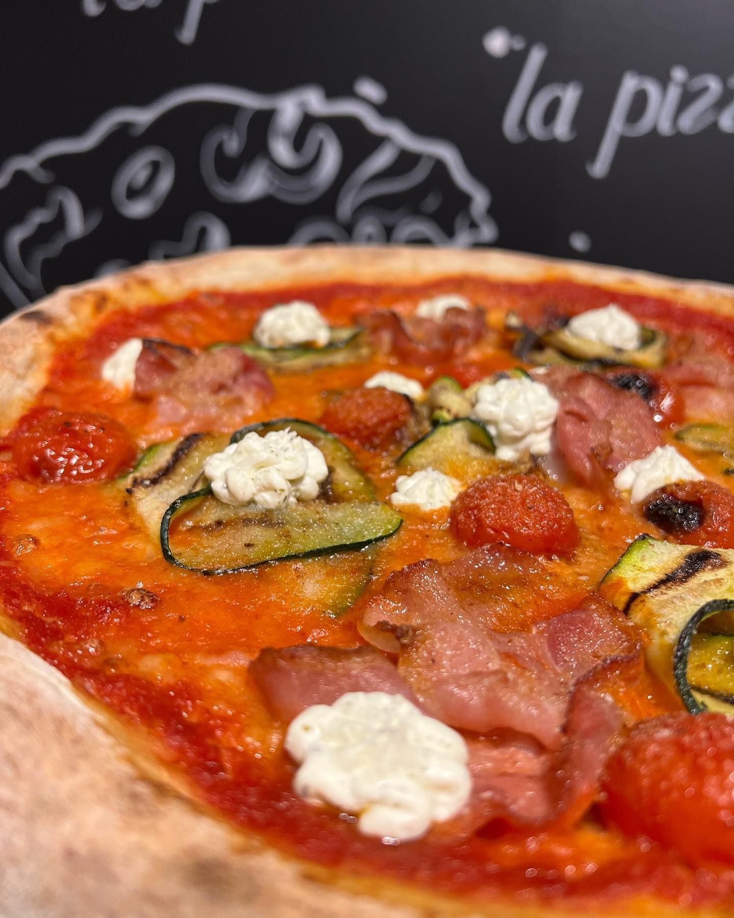 Un primo piano di una pizza con pomodori, zucchine e formaggio su un tavolo.