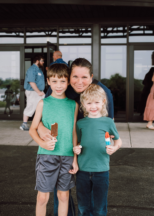 Two children holding drinks stand smiling in front of a building entrance.