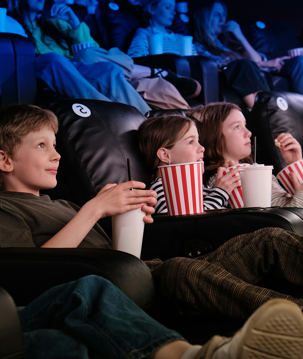 Children watching a movie in a theater, holding popcorn and drinks in red-and-white striped containers