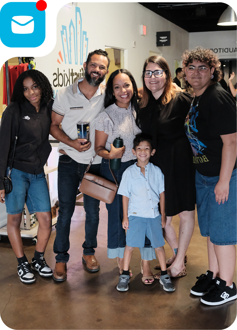 Group of six smiling people posing indoors, with one child standing in front.