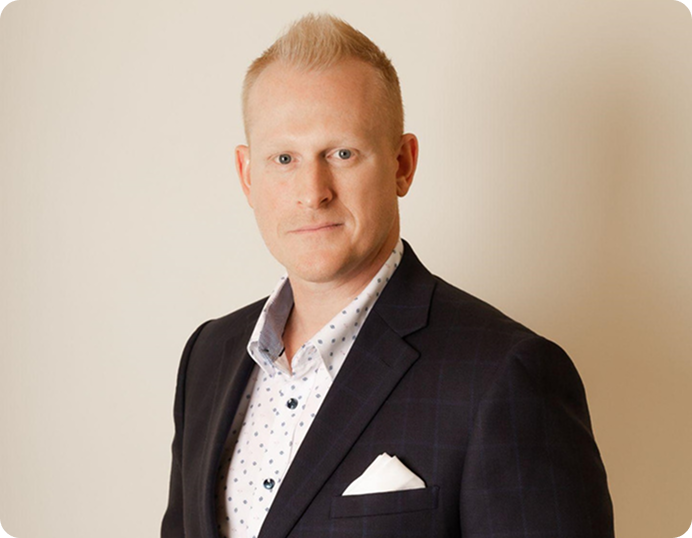 Portrait of a person in a dark blazer and patterned shirt against a beige background