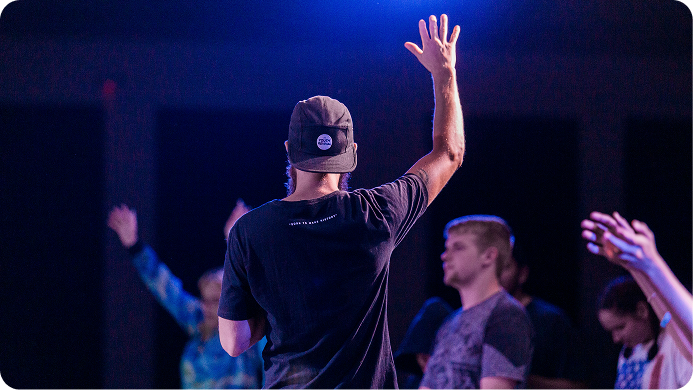 Person on stage raising a hand during a purple-lit event, with others blurred in the background