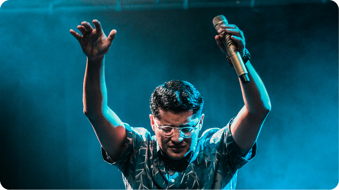 Singer with raised arms and microphone on a blue-lit stage