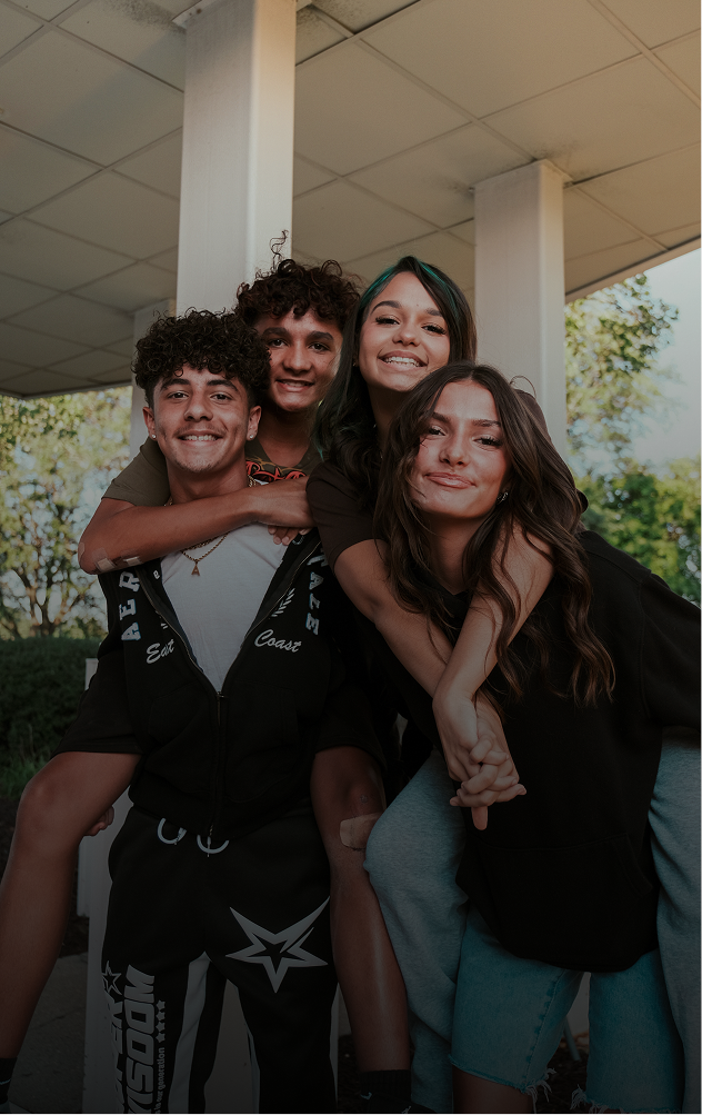Four friends smiling and posing together outdoors under a covered walkway