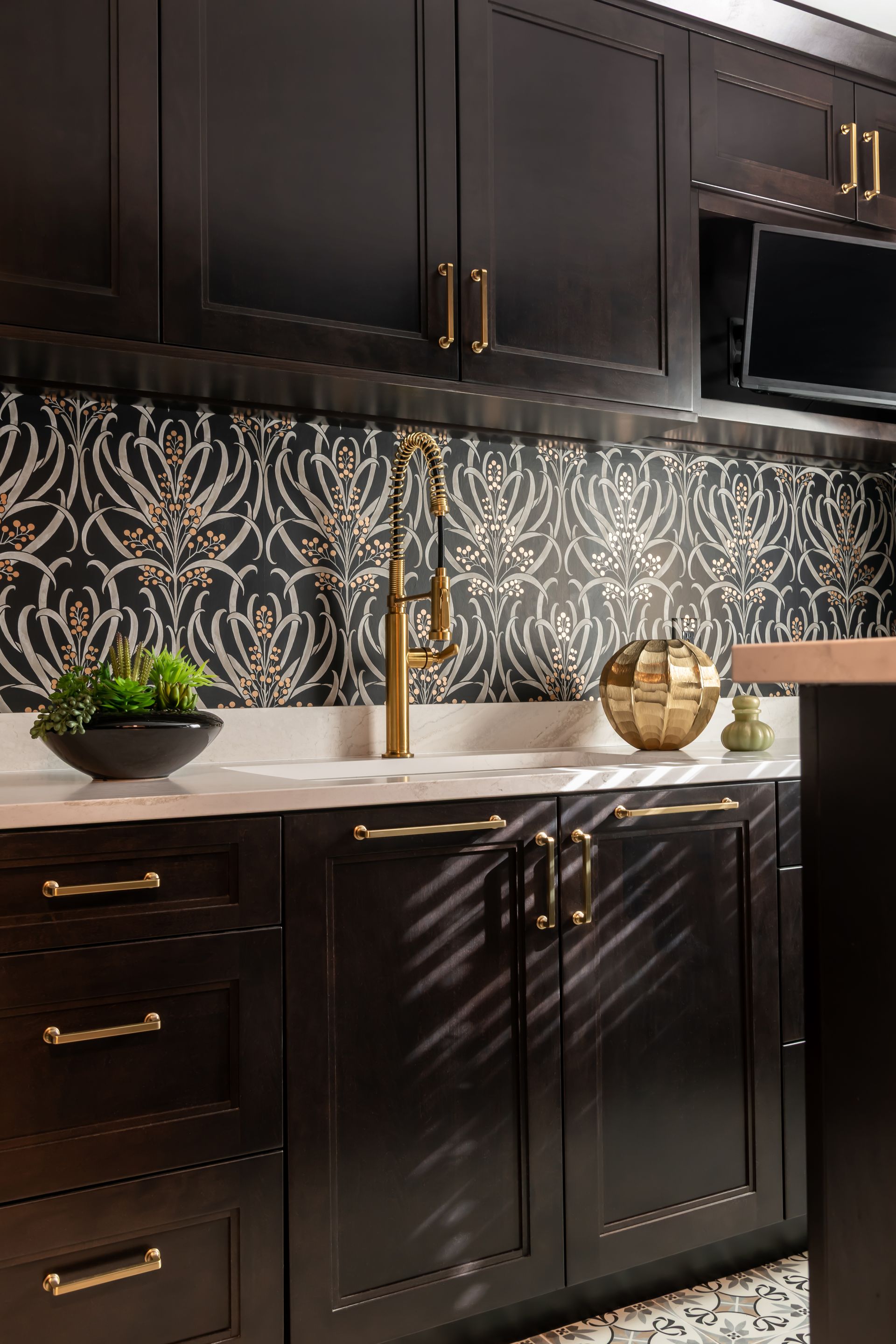 A kitchen with black cabinets and gold handles and a sink.