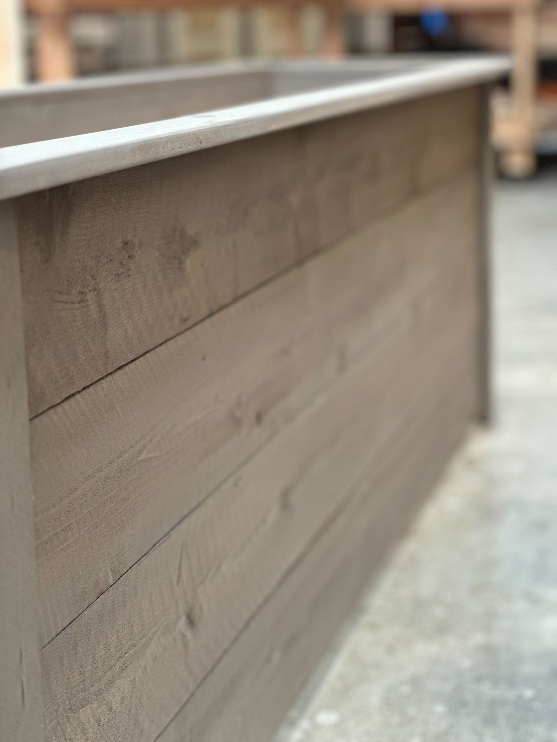 Close-up of a wooden ledge with a metal top, shown indoors on a concrete floor.