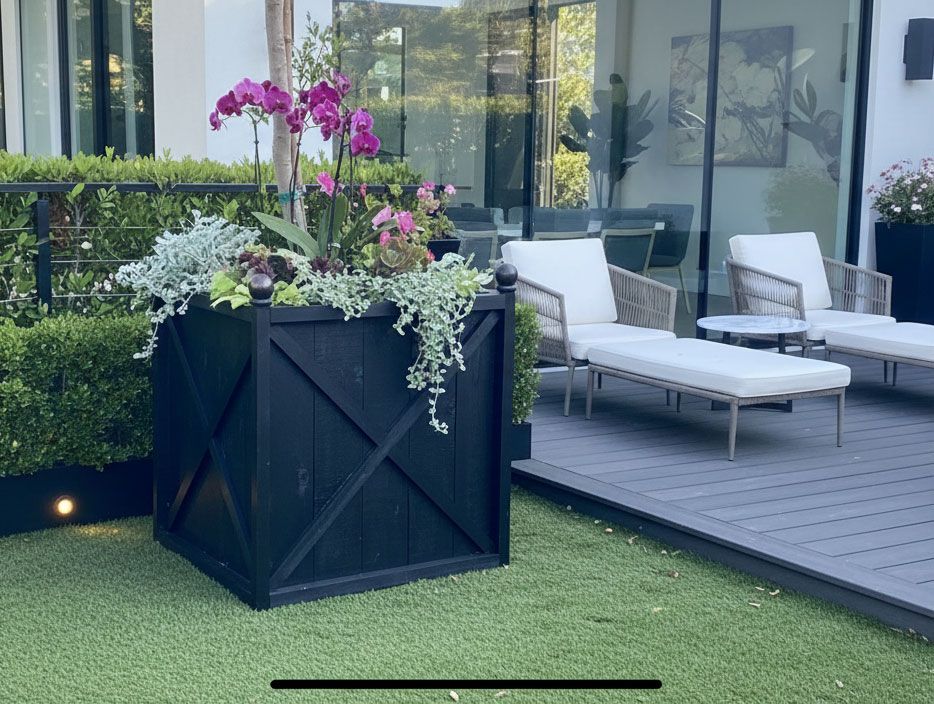 Patio with black planter of pink flowers beside white lounge chairs on a wooden deck