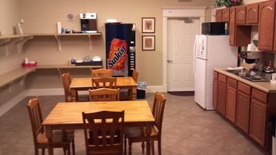 Break room with tables, chairs, cabinets, refrigerator, sink, and a large Pepsi vending machine.