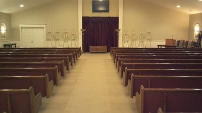 Empty church sanctuary with wooden pews facing a lectern and purple curtain at the front