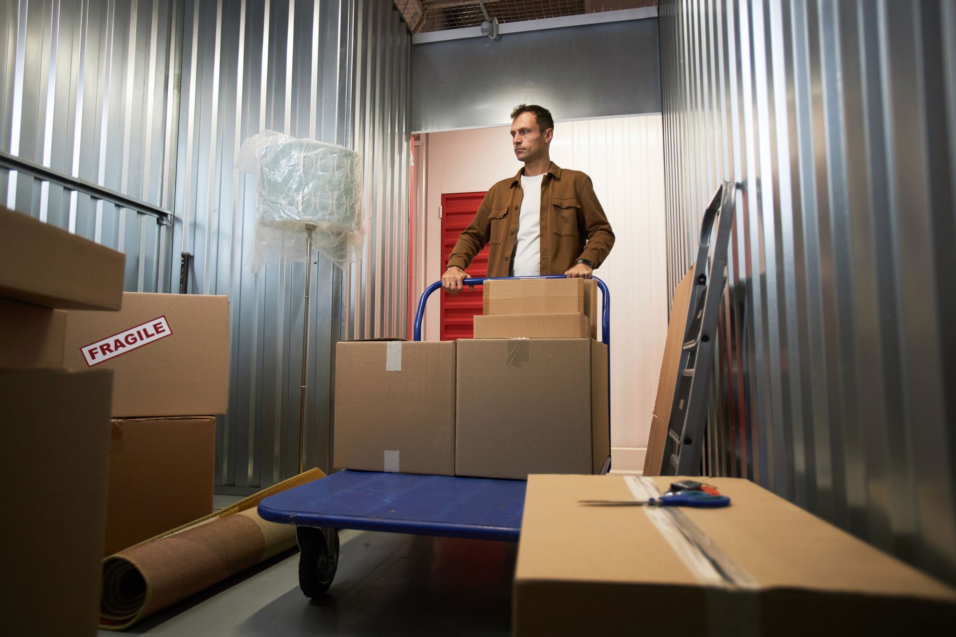 Man standing among stacked moving boxes in a corrugated metal storage unit