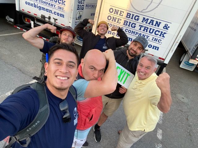 A group of men are posing for a picture in front of a moving truck.