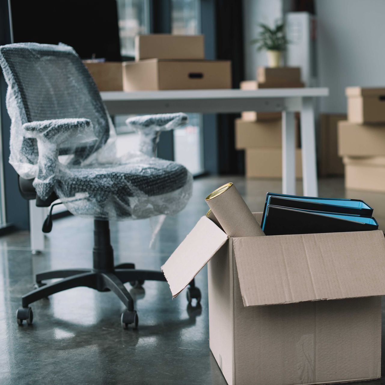 An office chair is wrapped in plastic next to an open cardboard box