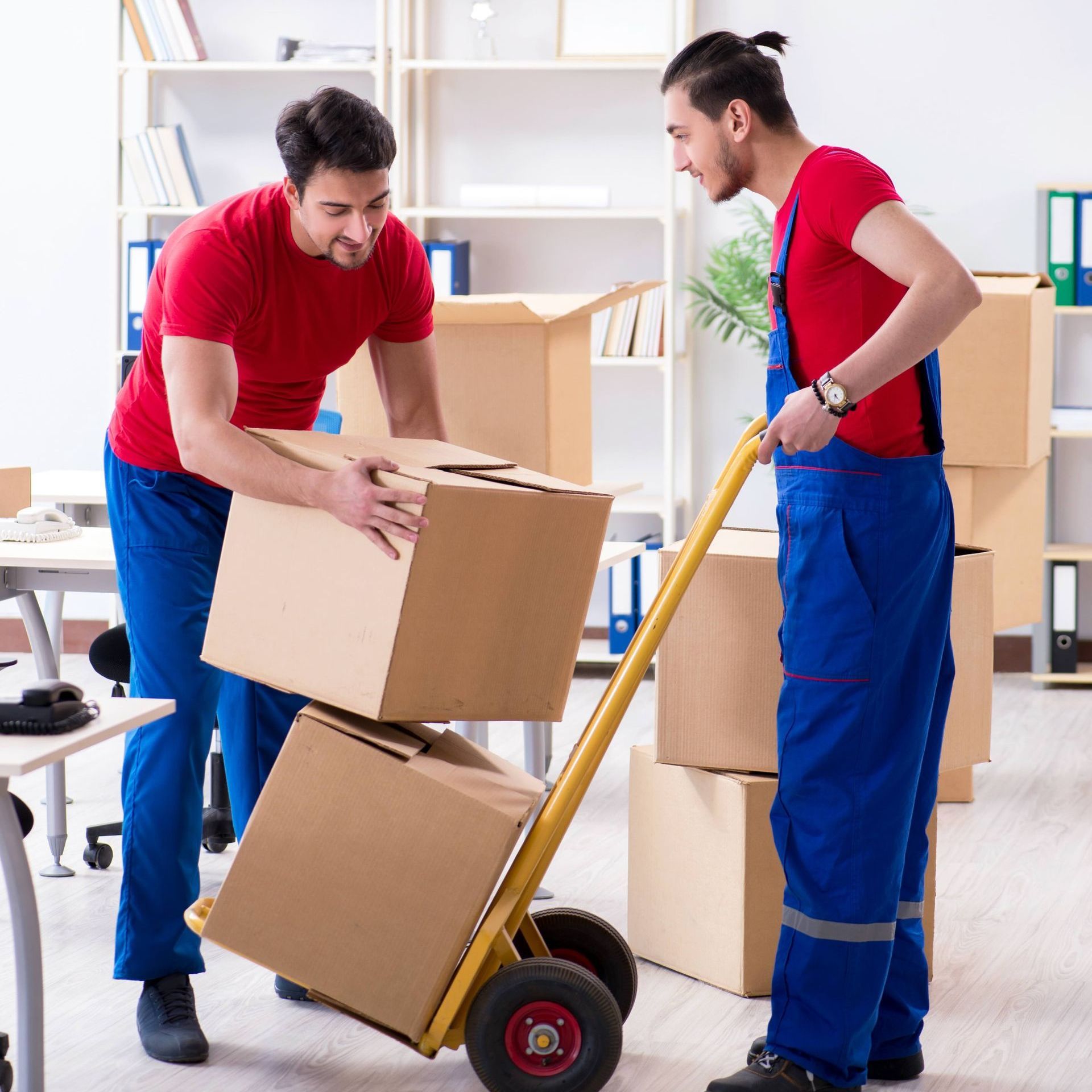 Two men are moving boxes on a dolly in an office.