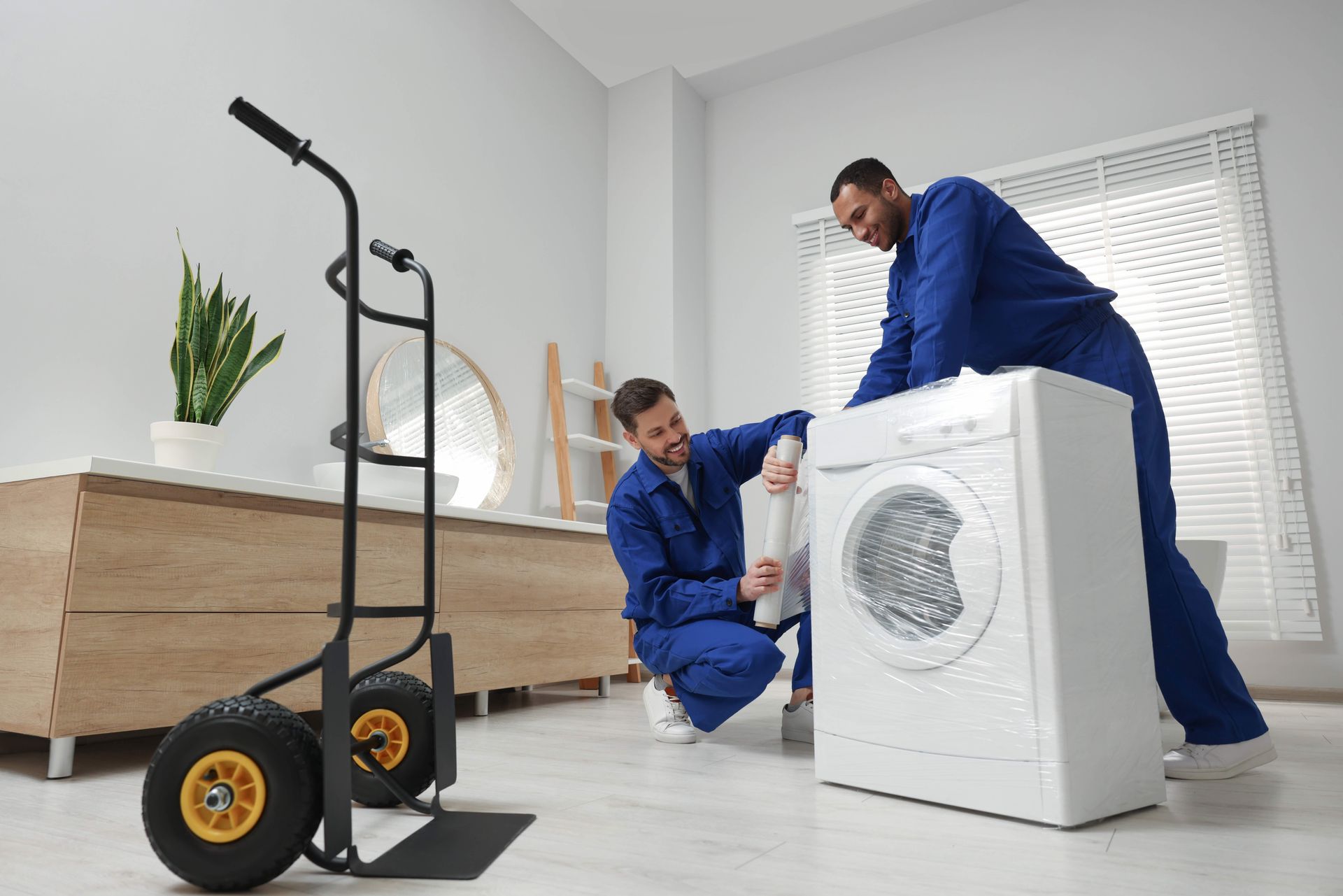 two men wrapping a washing machine with plastic wrap