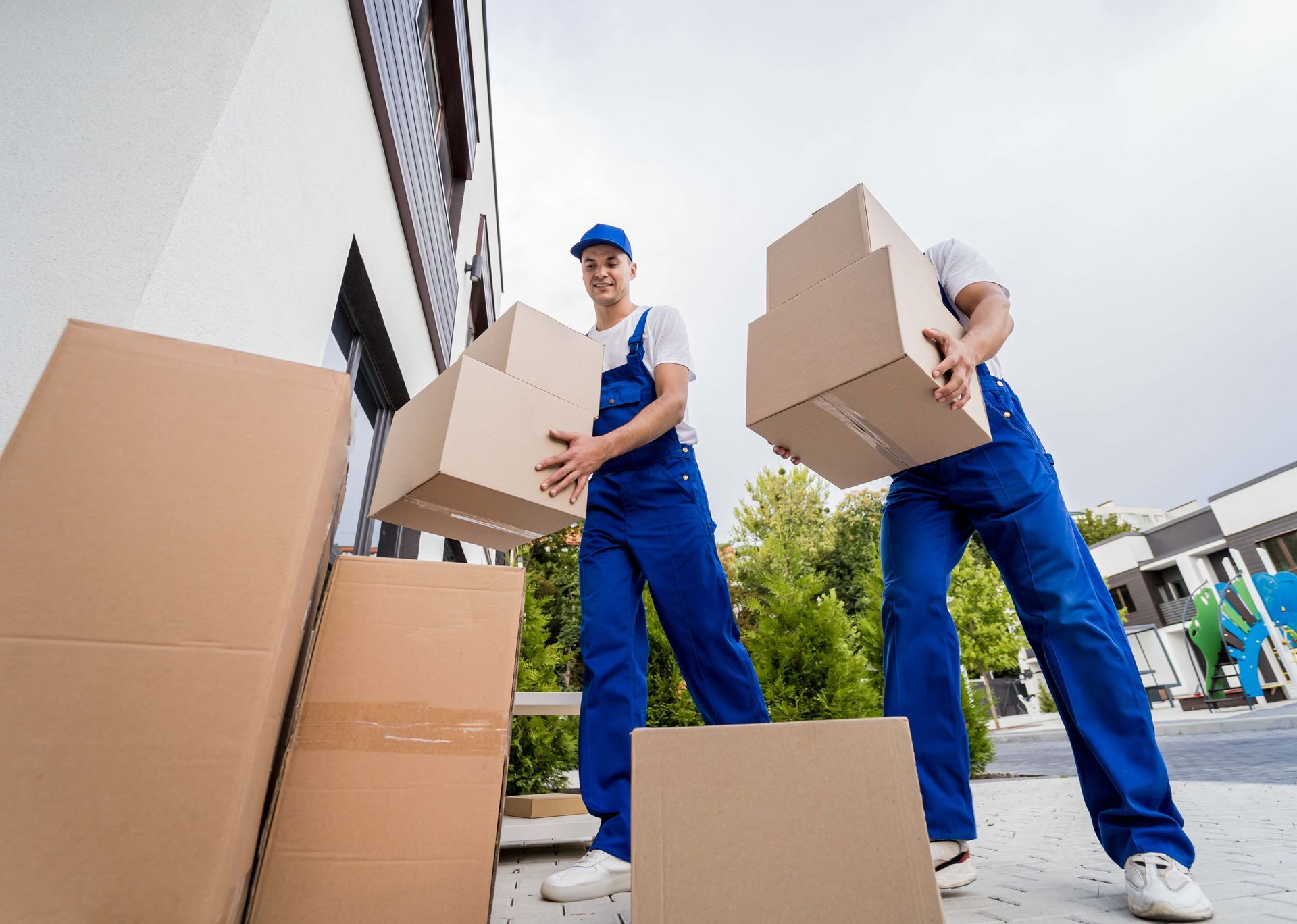 two men in blue overalls are carrying cardboard boxes