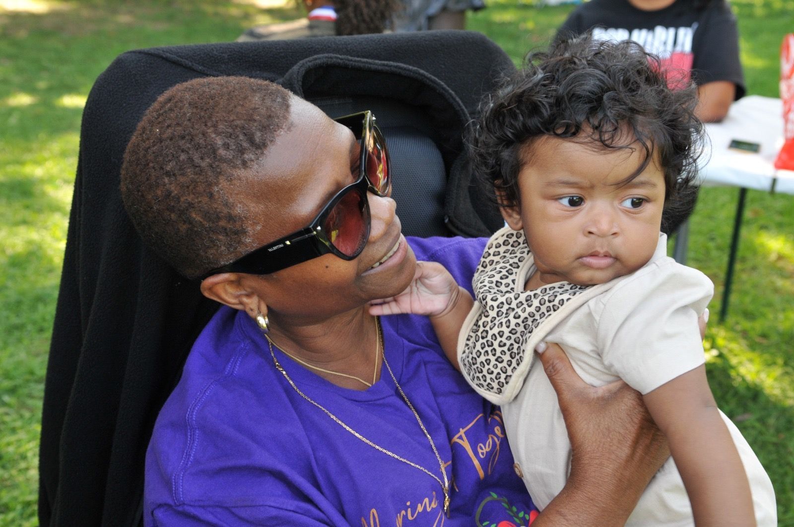 Adult holding a toddler outdoors at a park, both looking off to the side.