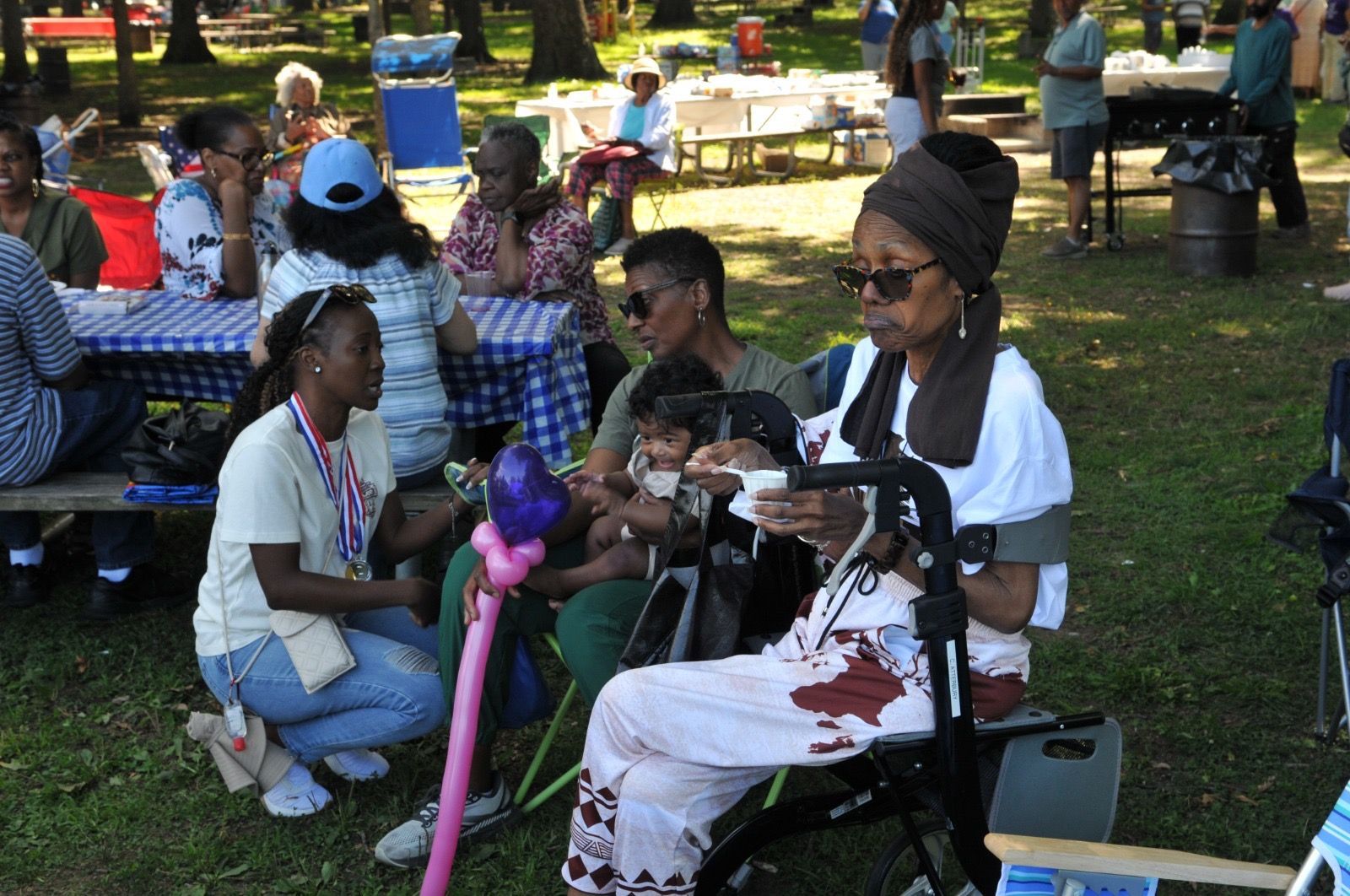 People relaxing at a park picnic, with one person in white seated on a wheelchair playing with a child.