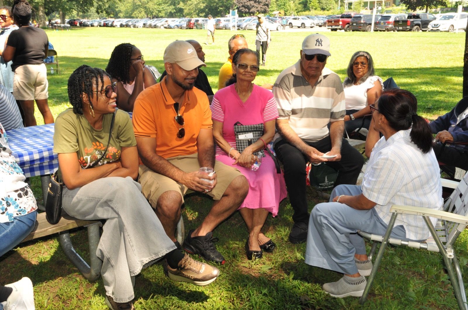 People sitting in a circle on folding chairs at a sunny outdoor park gathering
