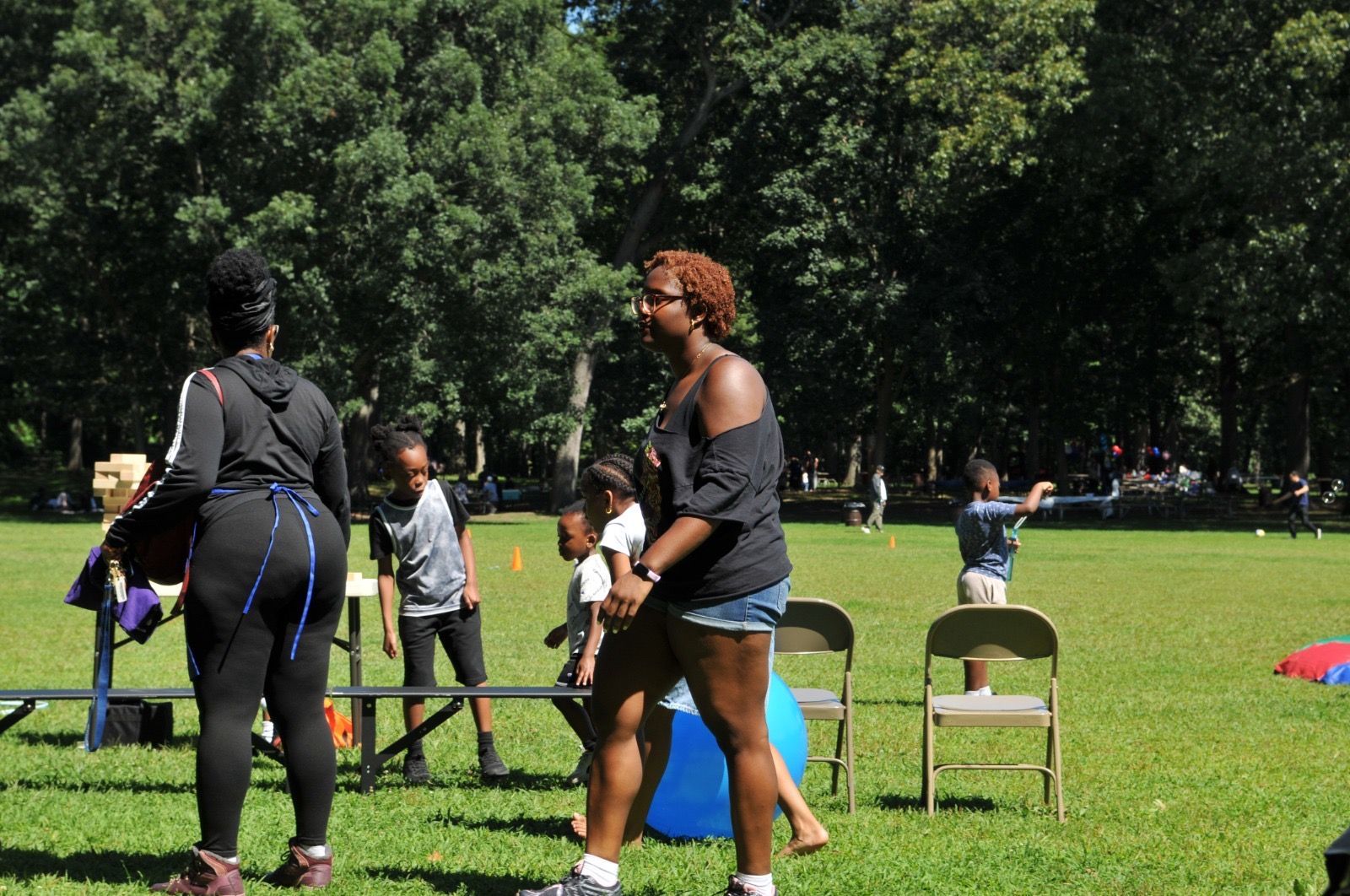 People exercising on grass in a park, with trees and folding chairs in the background.
