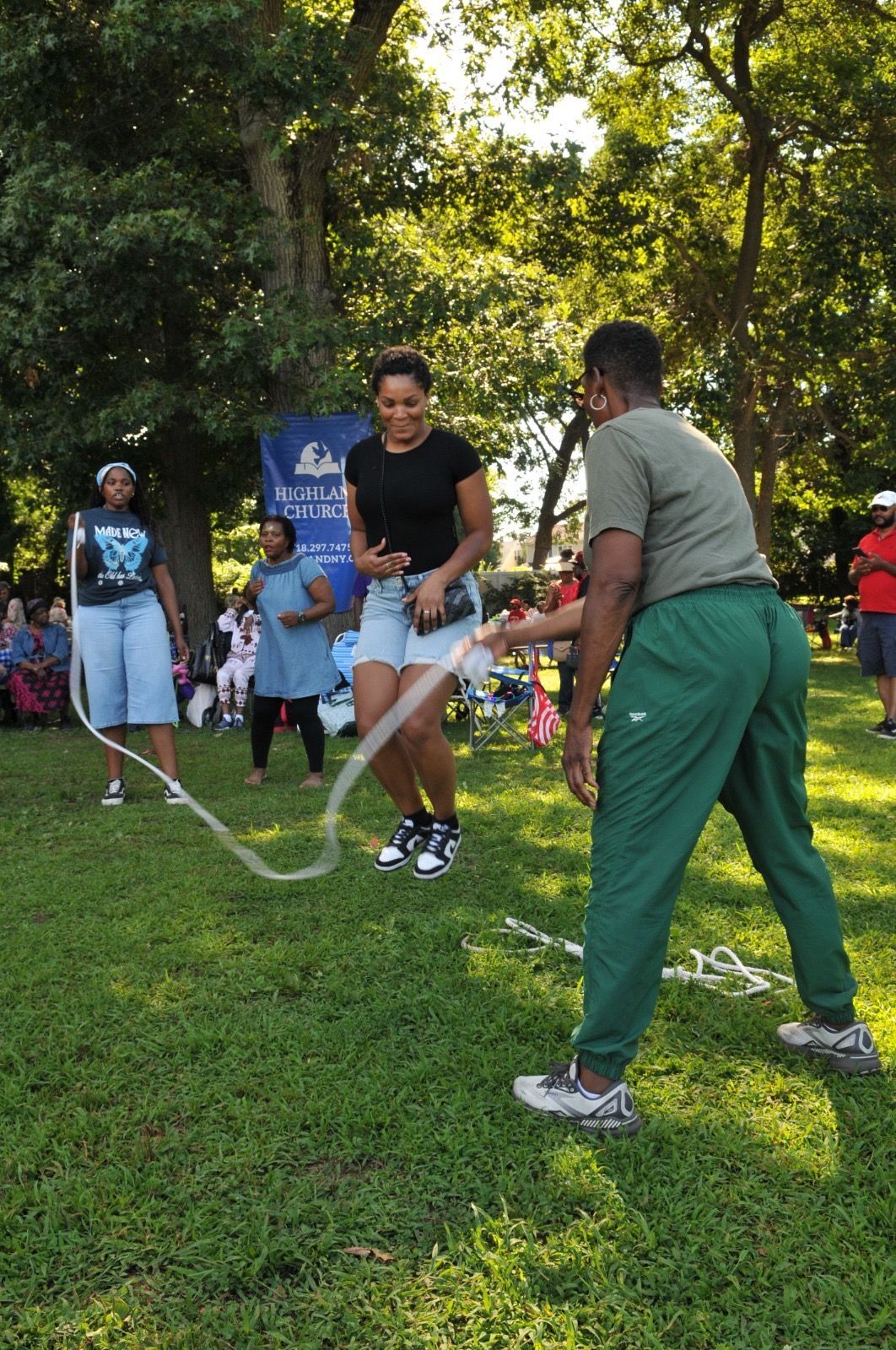 People jumping rope on a grassy field with trees in the background