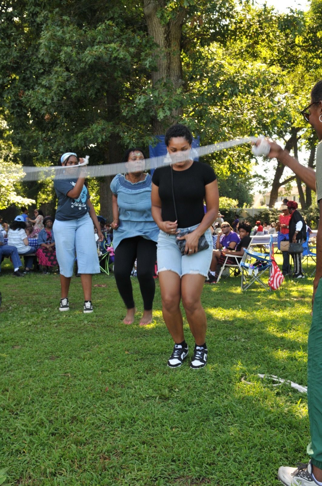 People pulling on a rope during an outdoor game in a park, with spectators and trees in the background.