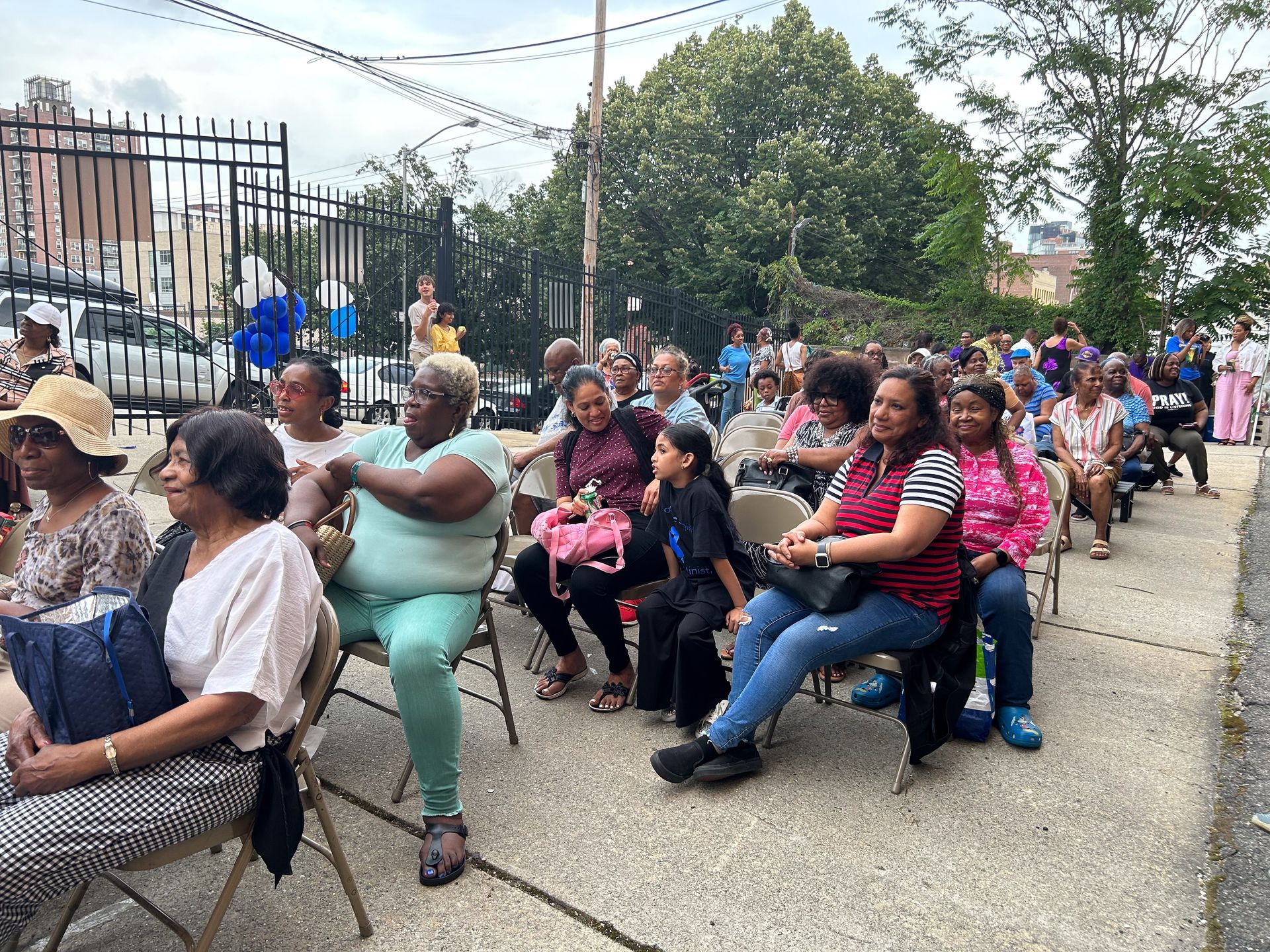 A large group of people are sitting in folding chairs outside.