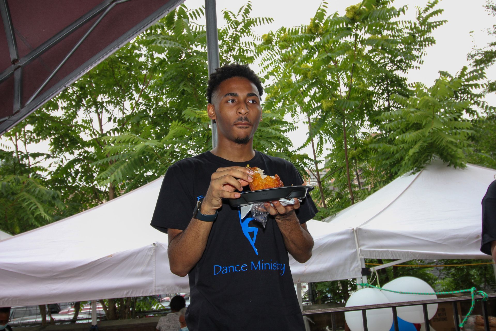 A man in a black shirt is holding a plate of food in his hands.