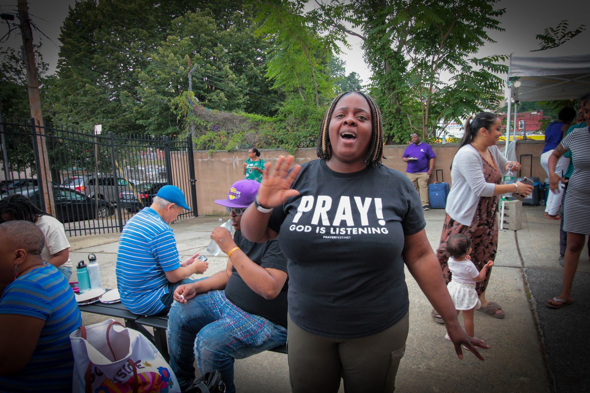 A woman wearing a pray t-shirt is standing in front of a group of people.