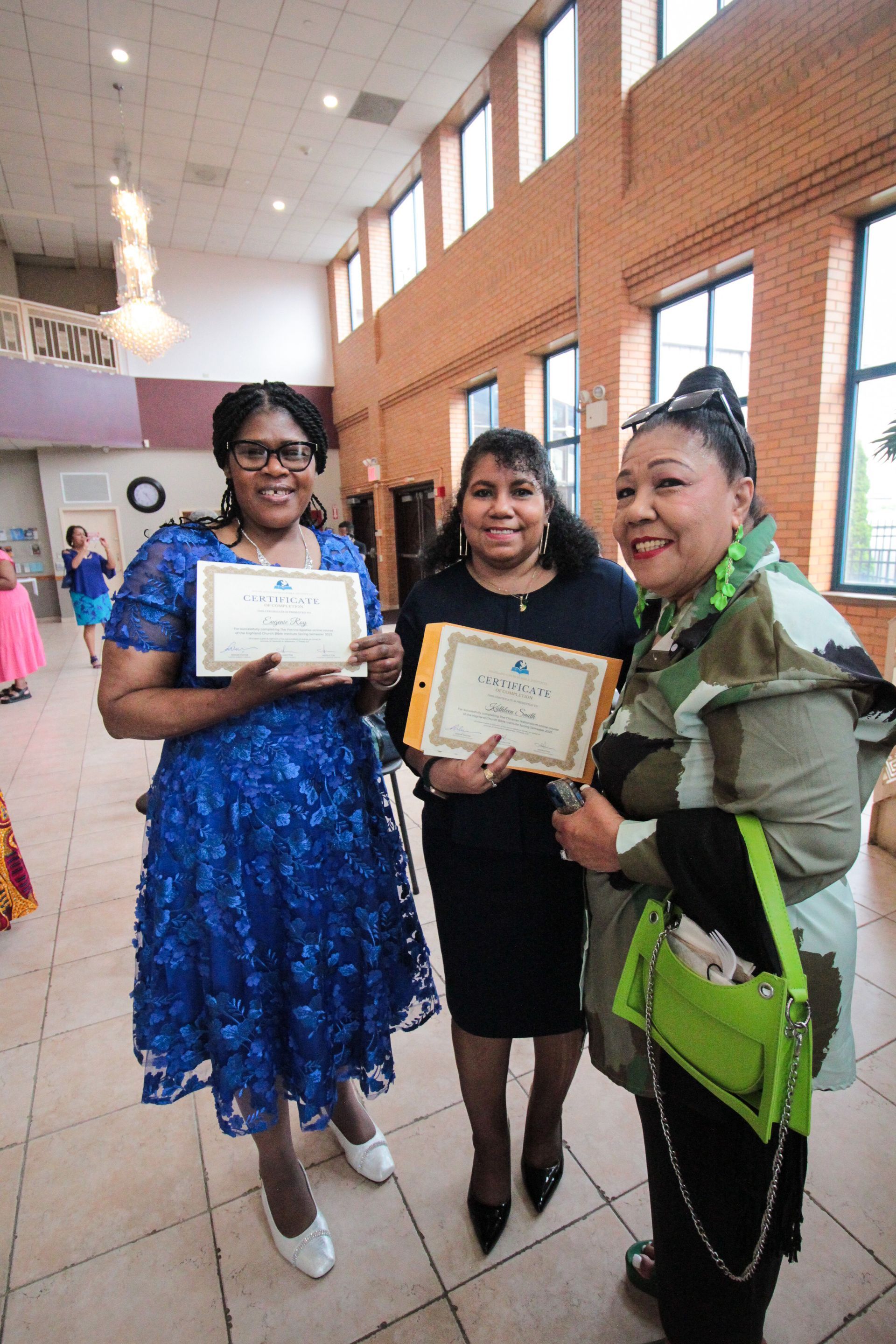 Three women are standing next to each other in a room holding certificates.