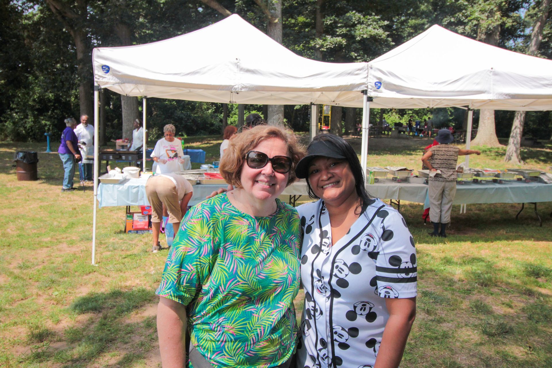 Two women are posing for a picture in front of a tent in a park.