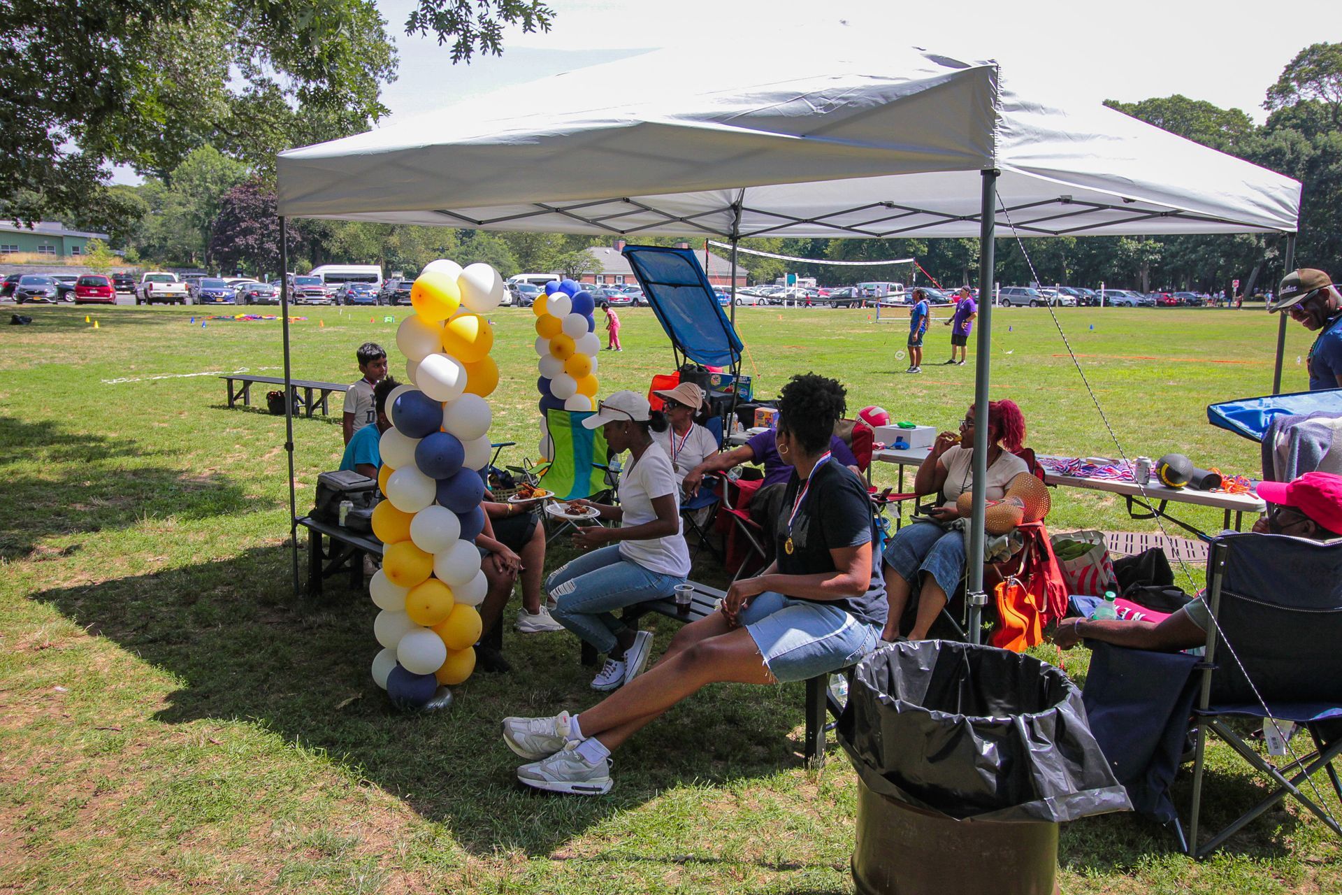 A group of people are sitting under a tent in a park.