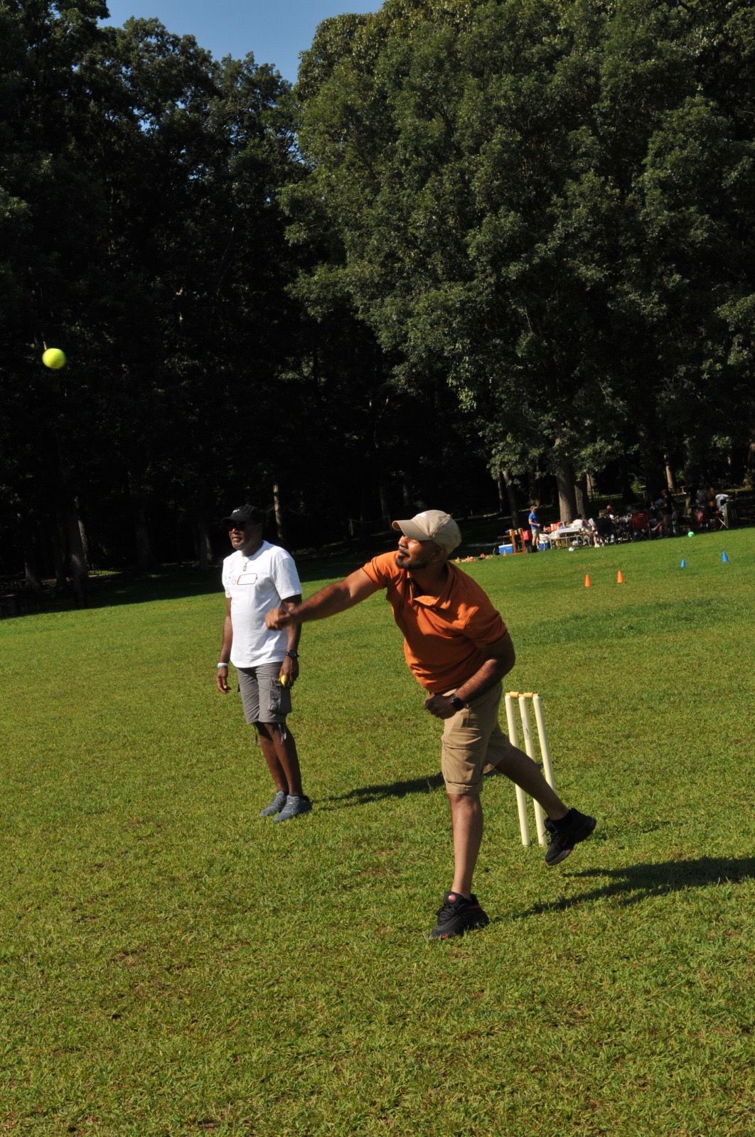 Two people playing catch on a sunny grassy field with trees in the background