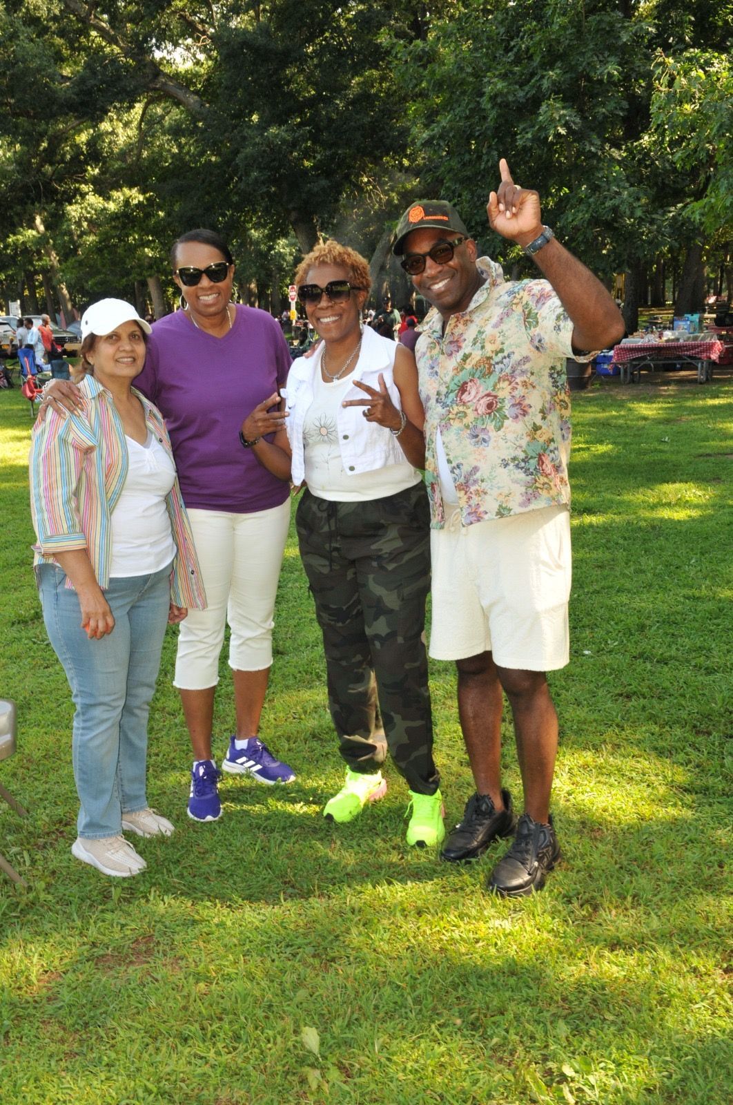 Four friends posing together on a sunny lawn, smiling and waving at the camera.